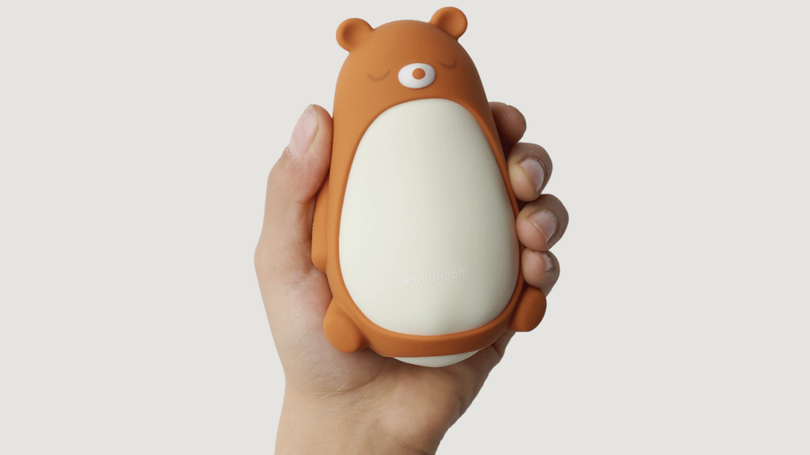A hand holds the Moonbird Moonbuddy. The device has the teddy sleeve on.