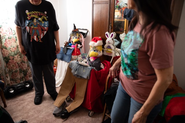 A man and woman stand next to stuffed toys with clothes laid out in front of them. 