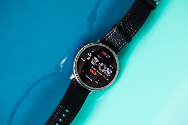 Angled view of the Amazfit Active 2 with a black leather strap undone. The watch sits atop a reflective blue acrylic background.