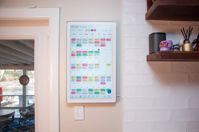 A large touchscreen calendar on a white tile wall.