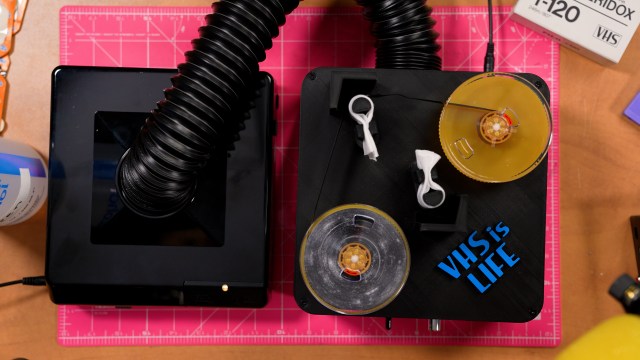 Top-down photo of two VHS spools resting on the VSH cleaner machine. The left spool is very moldy. White speckles all over the tape.