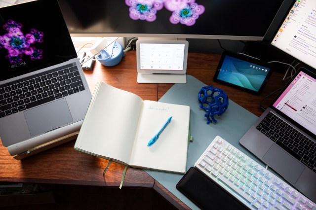 An open notebook on a desk surrounded by tech.
