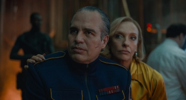 A man in a military suit sitting with a woman in a yellow blouse who has her hand on his shoulder.
