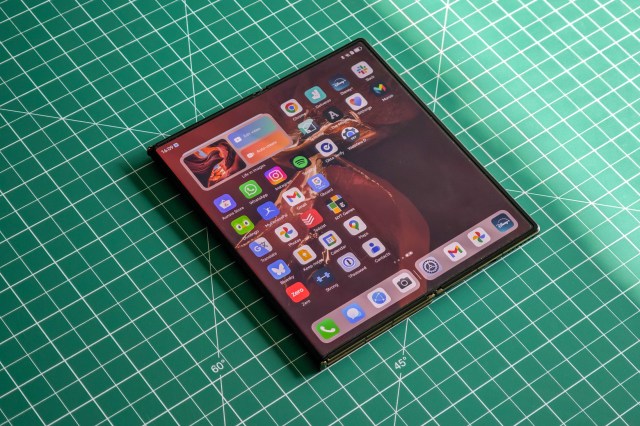 Huawei Mate XT flat on a green table partially unfolded.