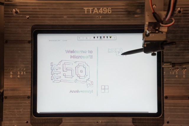 A robot creates a sketch of Microsoft’s 50th anniversary logo on a Surface Pro tablet.