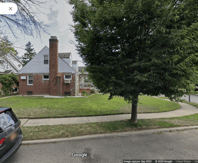 A suburban home with a plain, grassy lawn and a large tree on the periphery.
