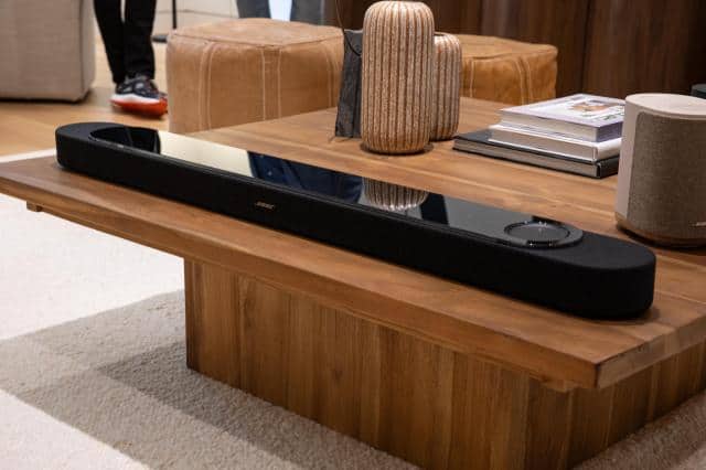 The Bose Lifestyle Ultra Soundbar in black on a wooden coffee table.