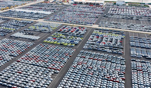 Hundreds of cars neatly arranged can be seen in an enormous parking lot from above. 