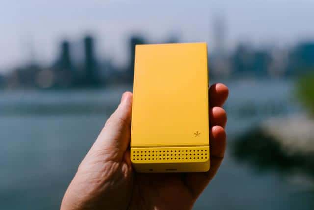 A yellow flip phone, closed, in front of a skyline.