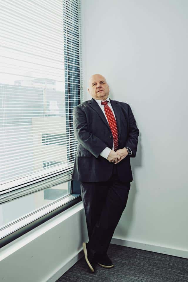 Buddy Rizer, an older man wearing a suit, poses for a portrait near the window in his office.