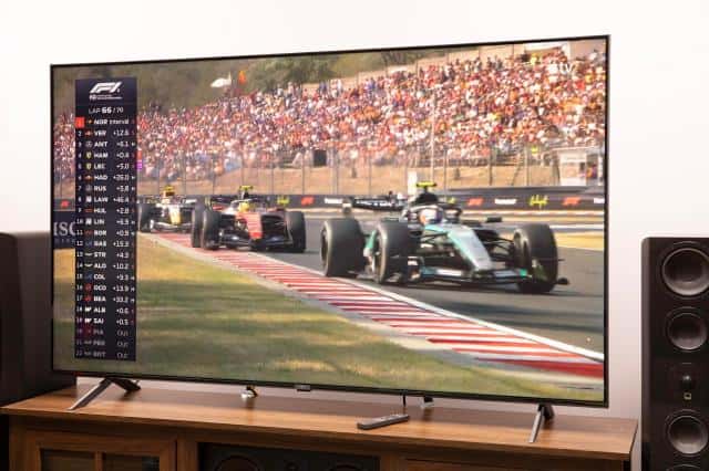 LG MRGB95B RGB LED TV on a TV stand showing a Formula 1 race.