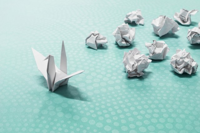 Image of an origami crane and several crumpled pieces of paper to represent success from failure.