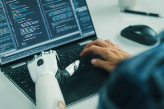 Imagen de una mano robótica y una mano humana trabajando juntas en un portátil con código en la pantalla. Post sobre Vibe Coding y su relación con la IA.