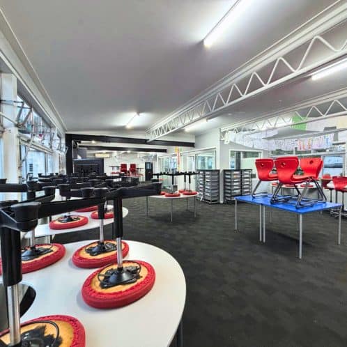 Stacked chairs and tables in a bright, modern indoor space with large windows, designed for seminars, workshops, or training sessions, featuring flexible seating arrangements and multimedia equipment.