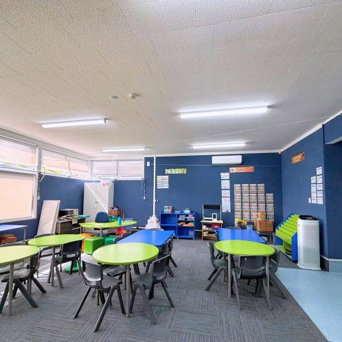 Bright learning classroom with colourful tables and chairs, educational materials on blue walls, and natural light from windows, ideal for early childhood education.