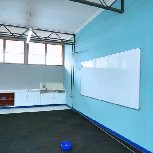 Empty classroom with whiteboard and storage cabinets, featuring bright natural light from large windows, educational space for teaching and learning, modern school interior.