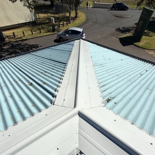 Corrugated metal roof with white flashing and some debris, outdoor commercial building roof in Auckland, New Zealand.