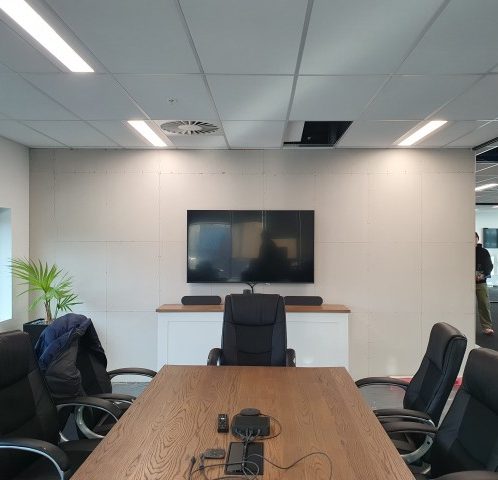 Modern corporate meeting room with a large wooden table, ergonomic chairs, and a flat-screen television for presentations and video conferences. Perfect for professional business meetings.