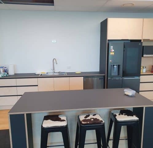 Modern kitchen area with black countertops and seating, featuring a fridge, microwave, and coffee station, ideal for office or workspace environments in New Zealand.