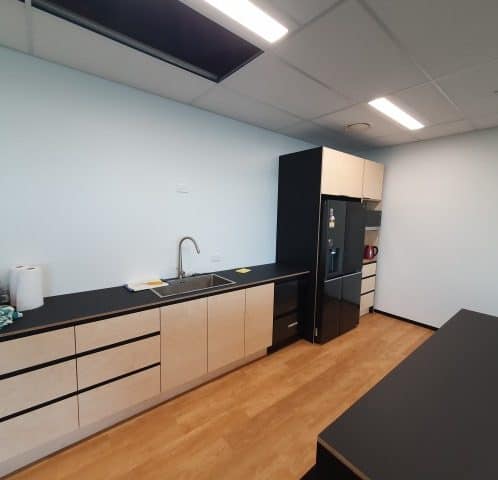 Modern minimalist kitchen with black countertops and beige cabinets in an office break room.