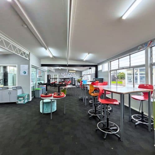 Keola indoor recreational area with high tables, colorful chairs, and large windows providing natural light for community activities and social gatherings.