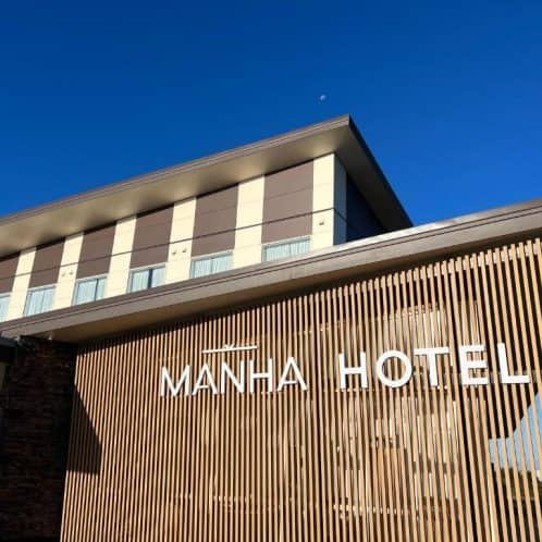 Contemporary Manha Hotel exterior with modern architectural design in New Zealand, featuring sleek wood accents and clear signage under a bright blue sky.