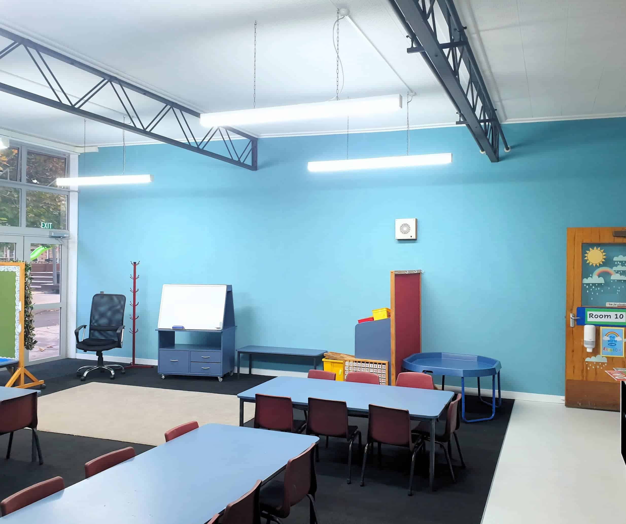 A colourful classroom with blue walls, child-sized tables and chairs, educational toys, and bright lighting, creating an engaging learning environment for young children at Keola childcare.