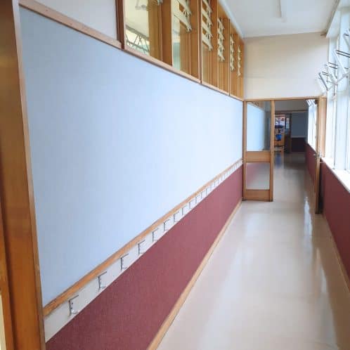 Bright indoor corridor with large windows, wooden accents, and hooks for hanging items, part of a professional office or educational facility. Well-lit space designed for organization and functionality.