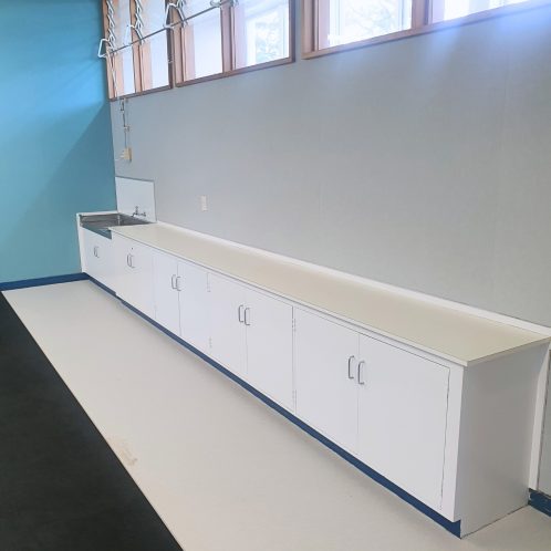 White commercial kitchen cabinetry and sink in a modern, minimalist kitchen setting.