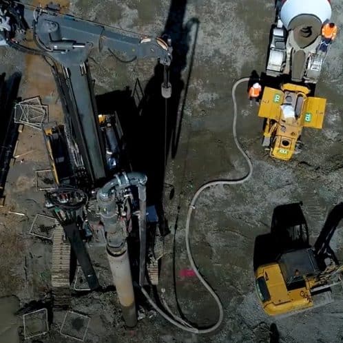 Drilling and construction equipment at a building site with workers in safety gear.