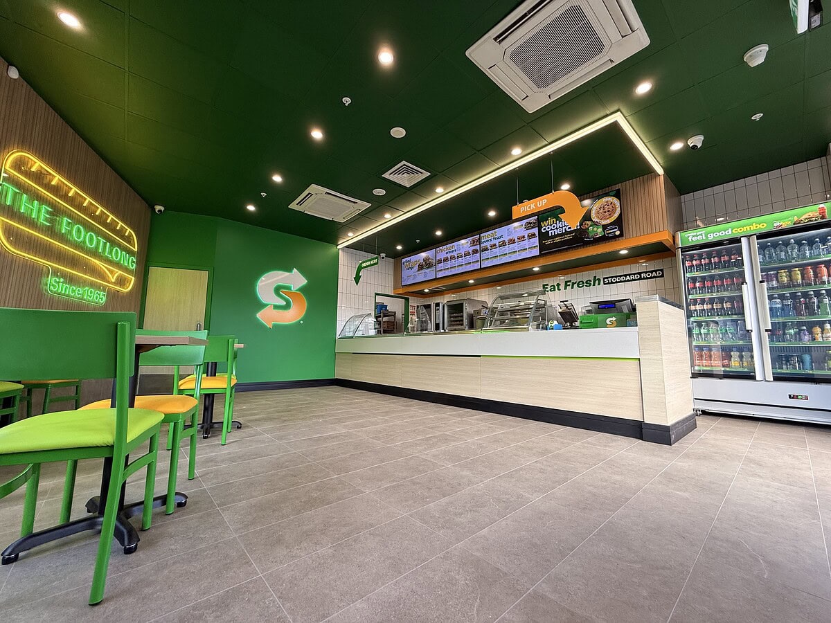 Wide-angle view of the completed Subway Fresh Forward 2.0 fitout showing seating, counter area, menu boards and feature lighting.
