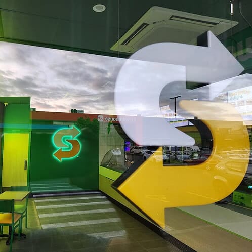 Window reflection showing illuminated Footlong neon sign and updated interior inside the newly refreshed Subway store.