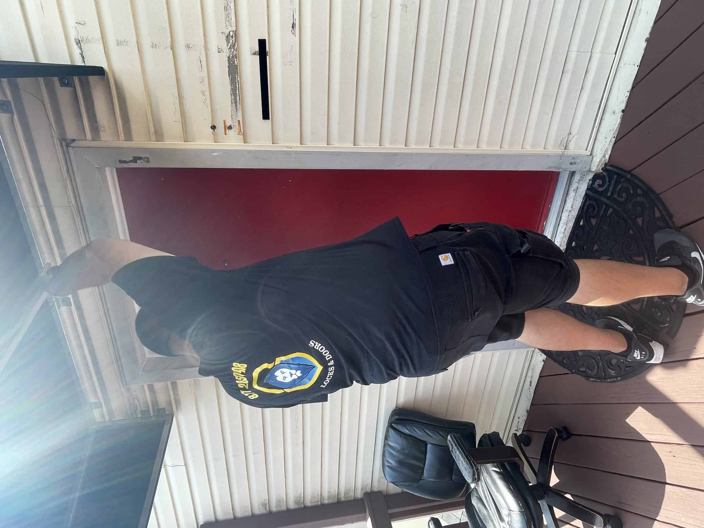 A Locksmith Annapolis Md Uniform Stands By A Red Door, Inspecting Door Problems