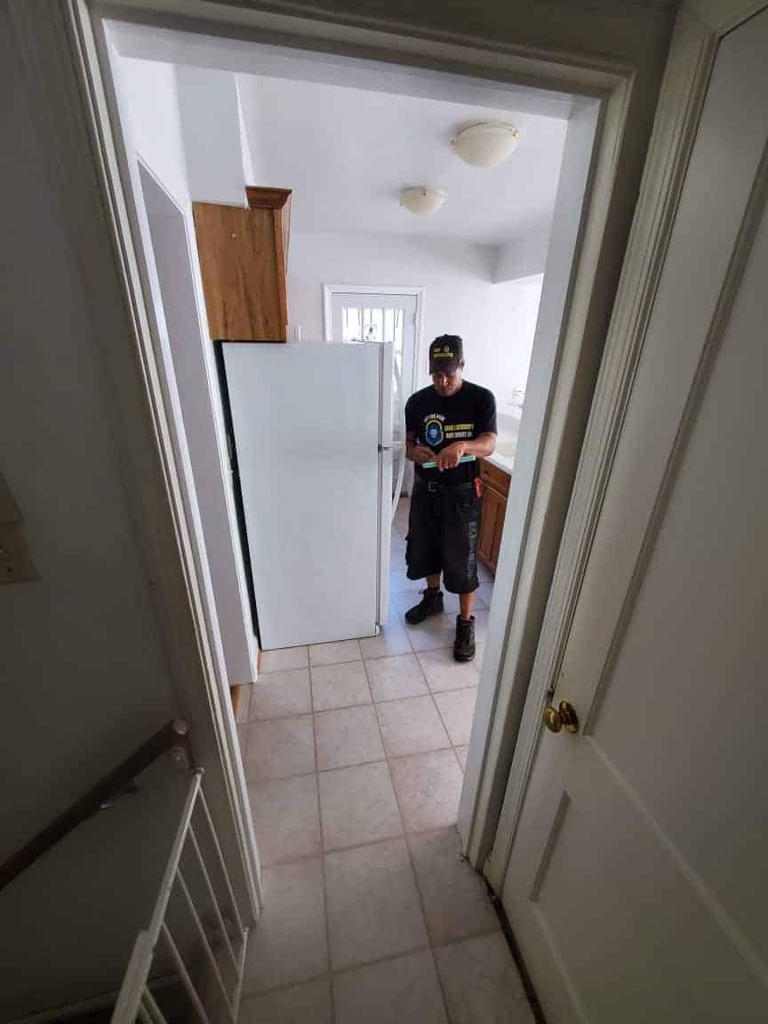 A Locksmith Md Uniform Beside The Refrigerator, Jotting Down Notes After Providing Repair Services.