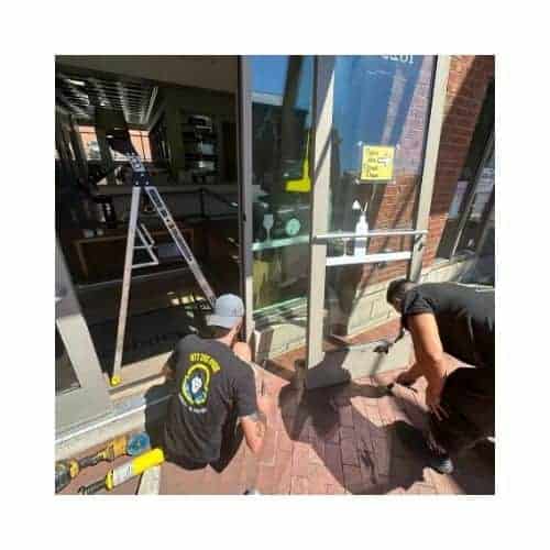 Two Locksmiths In Black Repairing The Storefront Door In Catonsville Md