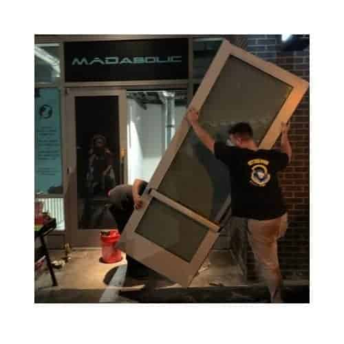 Two Locksmiths From King Locksmith And Door Inc. Lifting An Aluminum Door For Installation After Completing Repairs.