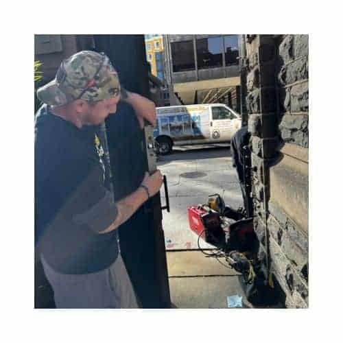 A Locksmith From King Locksmith, Wearing A Black Uniform And Hat, Installing A Door Latch On A Steel Door In Catonsville, Md