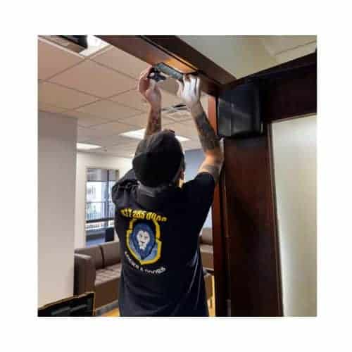 Technician From King Locksmith Repairing A Magnetic Lock On A Wooden Door Frame In A Commercial Building In Catonsville Md, With Tools And Clarksburg Seating Visible In The Background