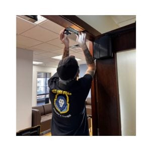 Technician From Kensington Locksmith Repairing A Magnetic Lock On A Wooden Door Frame In A Commercial Building In Kensington Md, With Tools And Seating Visible In The Background