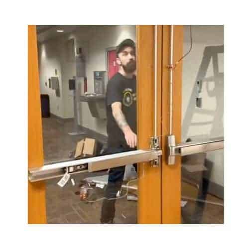 Wood-Framed Double Doors With Glass Panels Featuring A Panic Bar Mechanism And Visible Wiring For An Electronic Locking System, With A Locksmith From King Locksmith Working Behind The Door In A Commercial Or Institutional Building In Burtonsville Maryland