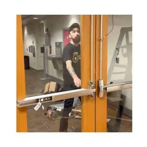 Panic Bar_ Exit Devices In Glen Burnie Maryland Technician From King Locksmith Repairing A Magnetic Lock On A Wooden Door Frame In A Commercial Building In Glen Burnie Md, With Tools And Seating Visible In The Background