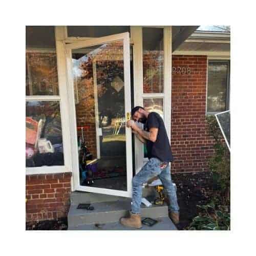 A Locksmith From King Locksmith And Doors Inc., Wearing A Black Uniform, Repairing A Storm Door In Burtonsville Md Using Complete Tools.