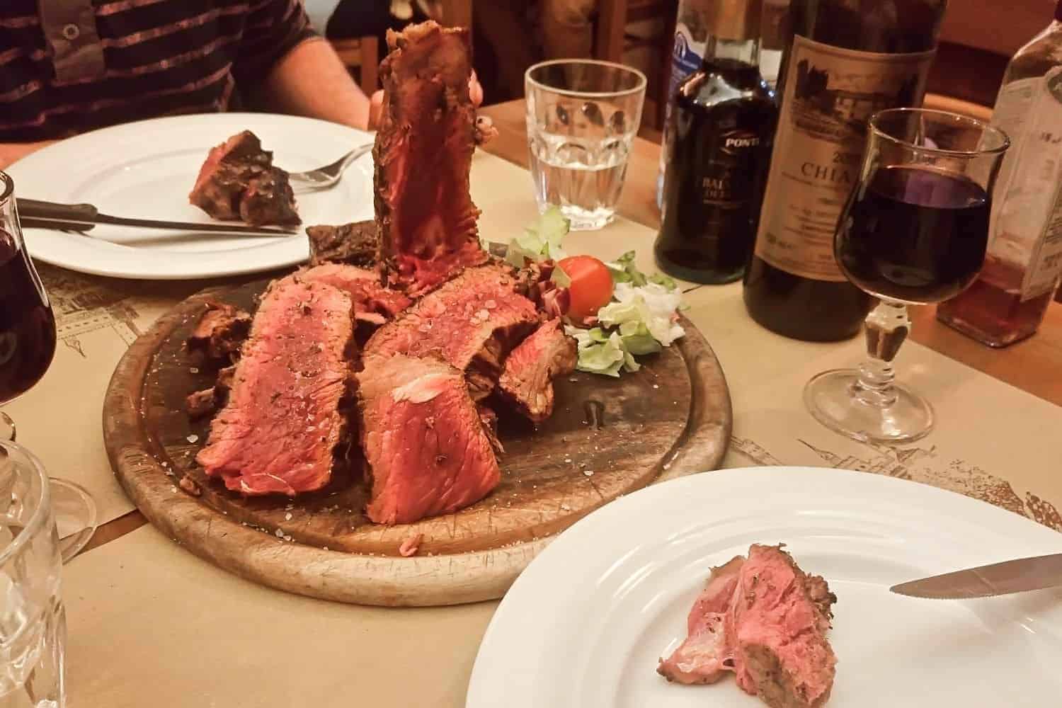 bistecca alla fiorentina in florence - steak with a bit of juices visible and wine glasses on the side