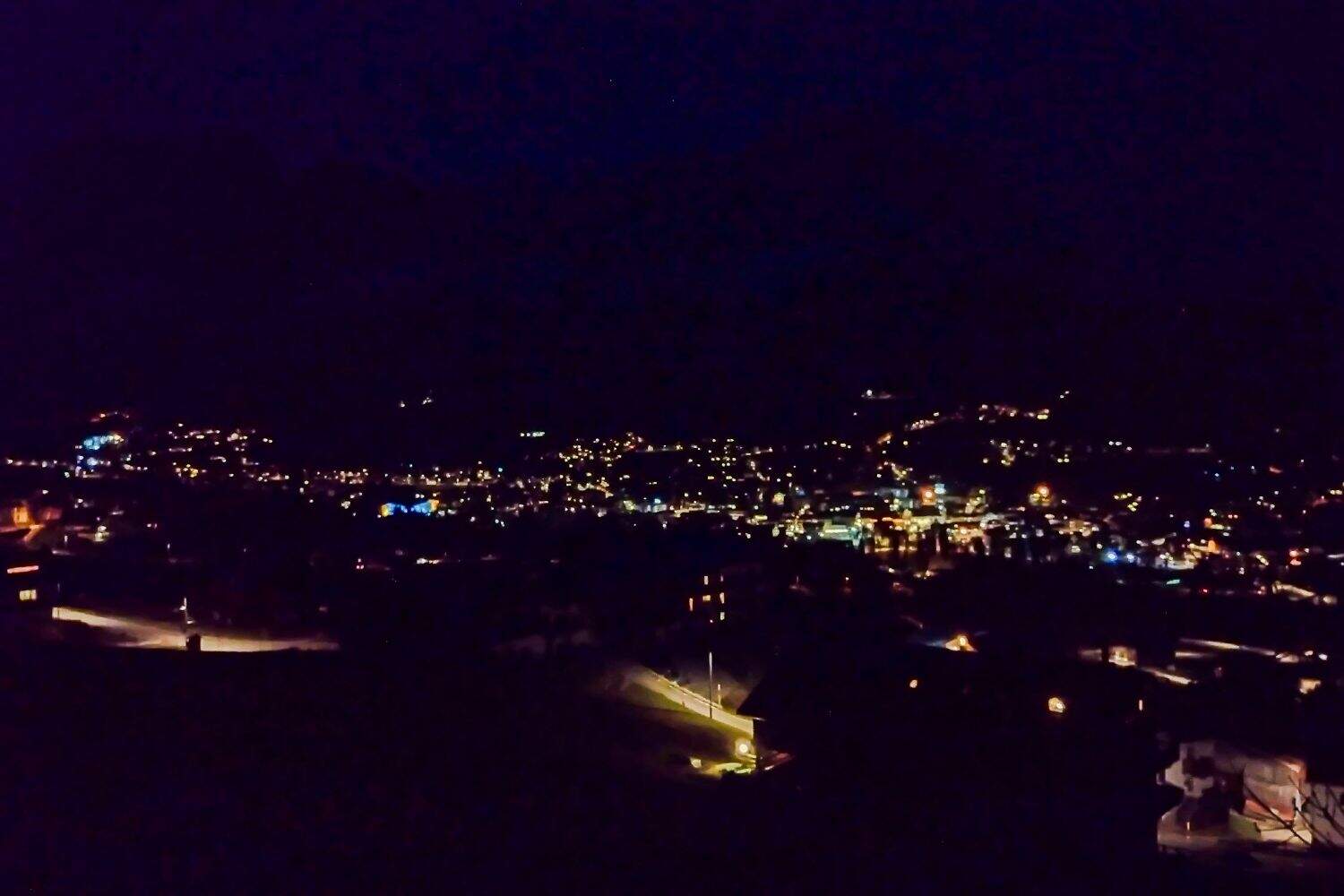 A night view of a town with scattered streetlights and building lights glowing in the darkness; the surrounding area is mostly dark, highlighting the illuminated town center.