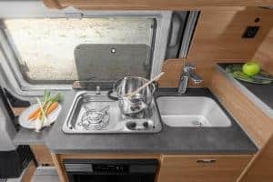 Gemütliche Küchenzeile im Moon Camper mit Mini-Gaskocher und Spüle für Camping und Roadtrip-Abenteuer.