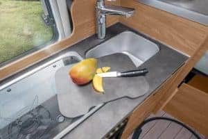 Frischer MANGO auf Küchenarbeitsplatte im Moon Camper, handliche Messer, kompakte Küchenzeile, moderne Campingküche in Wohnmobil.