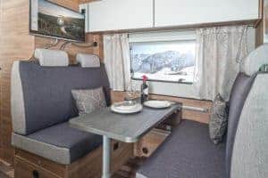 Gemütlicher Wohnbereich im Moon Camper mit Blick auf verschneite Berge, ideal für Campingurlaub in der Natur.