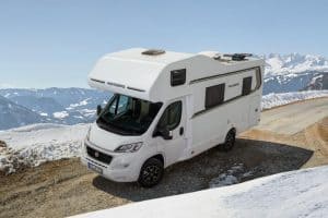 Campingbus mit Wohnmobil auf verschneiter Bergstraße in den Alpen.