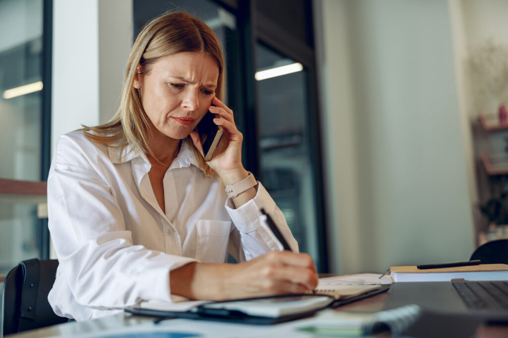 Concerned businesswoman on the phone taking notes at her desk, reflecting the stress of receiving a CIPA demand letter