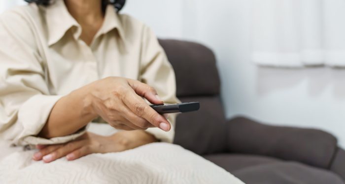 Elderly woman Watching smart TV and using remote controller Hand holding television audio remote control Middle age Asian woman movie Television series spending time at home.